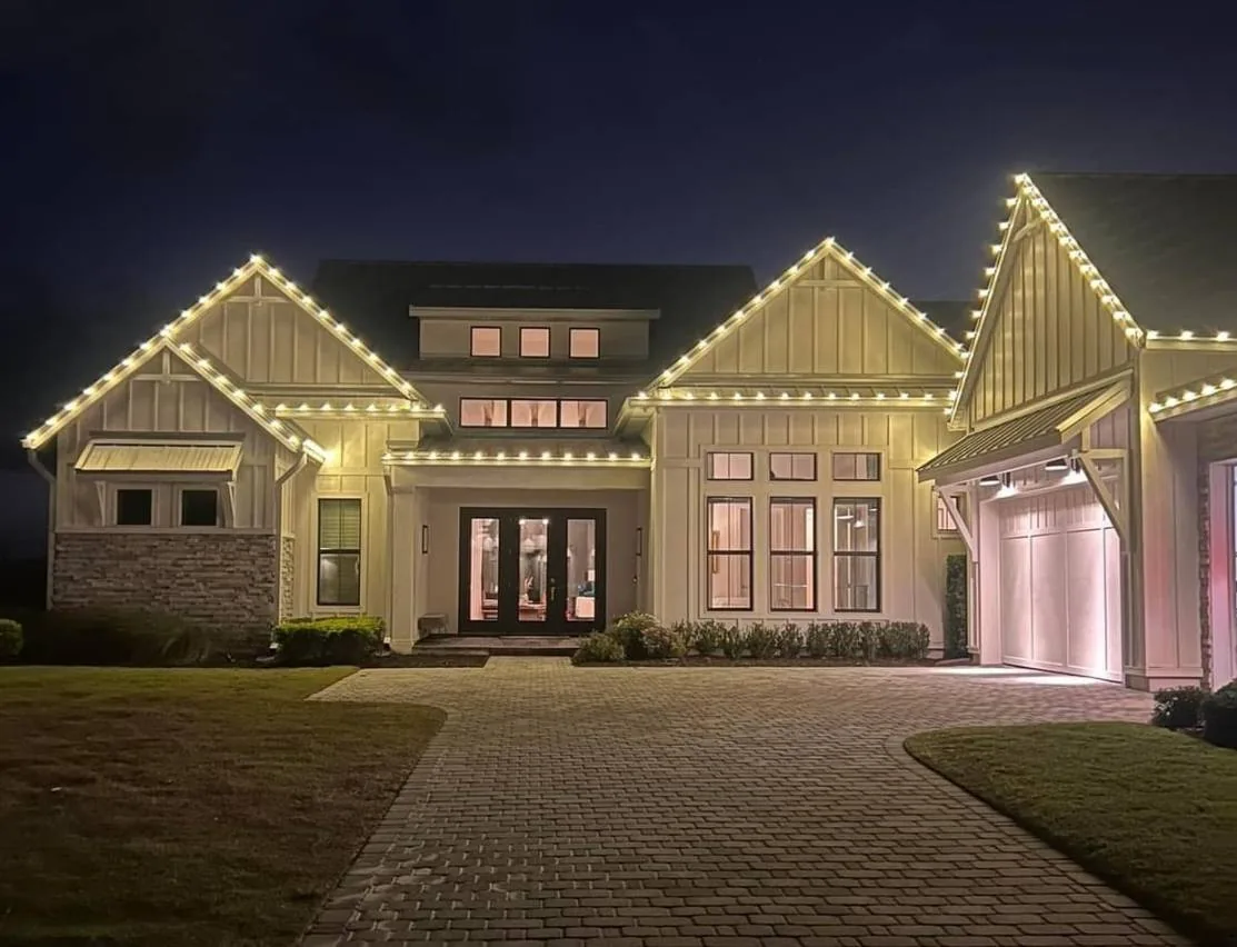 Modern farmhouse at night with warm-white lighting tracing each gable and the roofline.