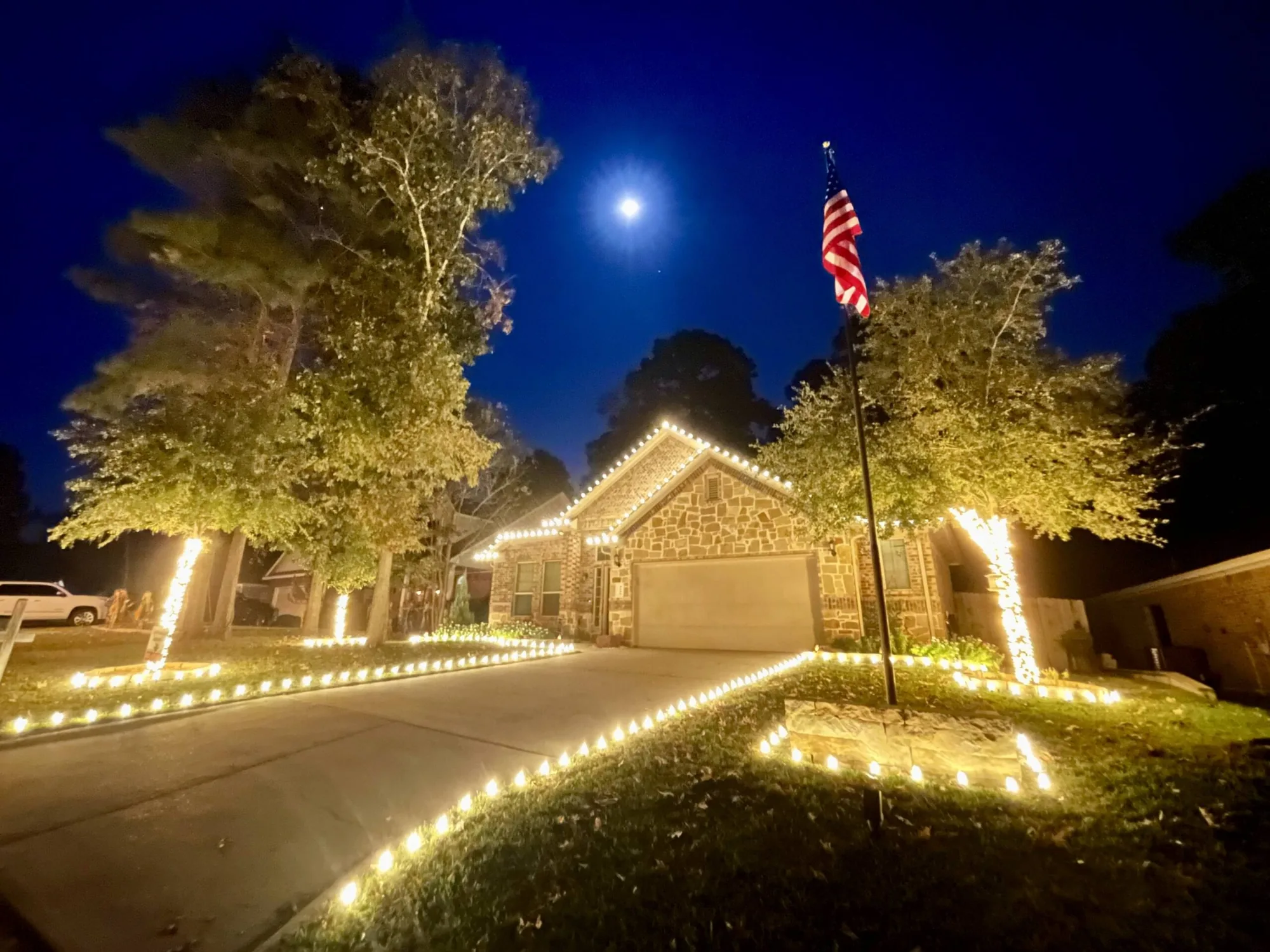 Single-storey Texas ranch home at night with wrapped tree trunks, a lit walkway and warm-white rooflines.